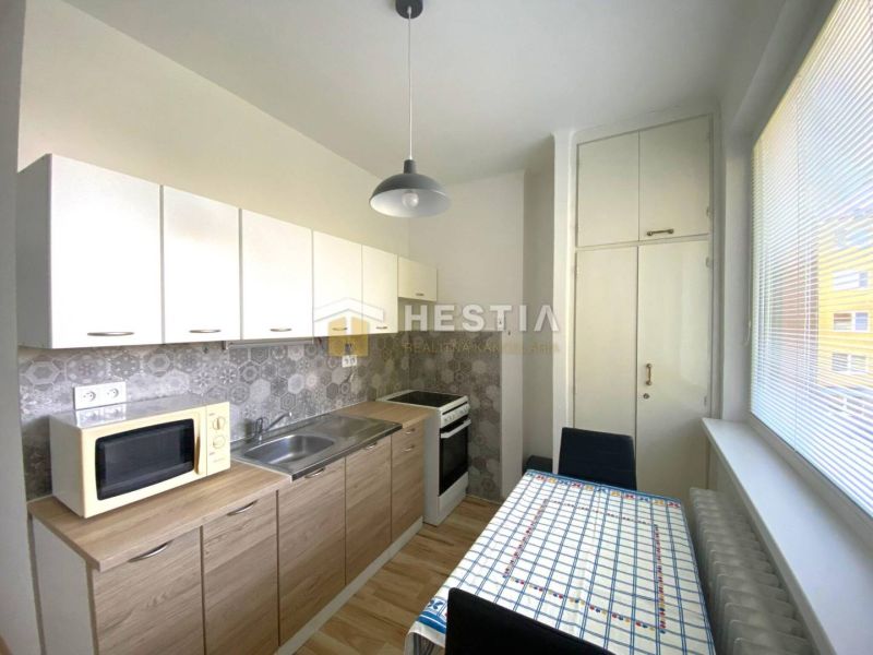 A kitchen with white cabinets and a wood-patterned floor in a two-room apartment.
