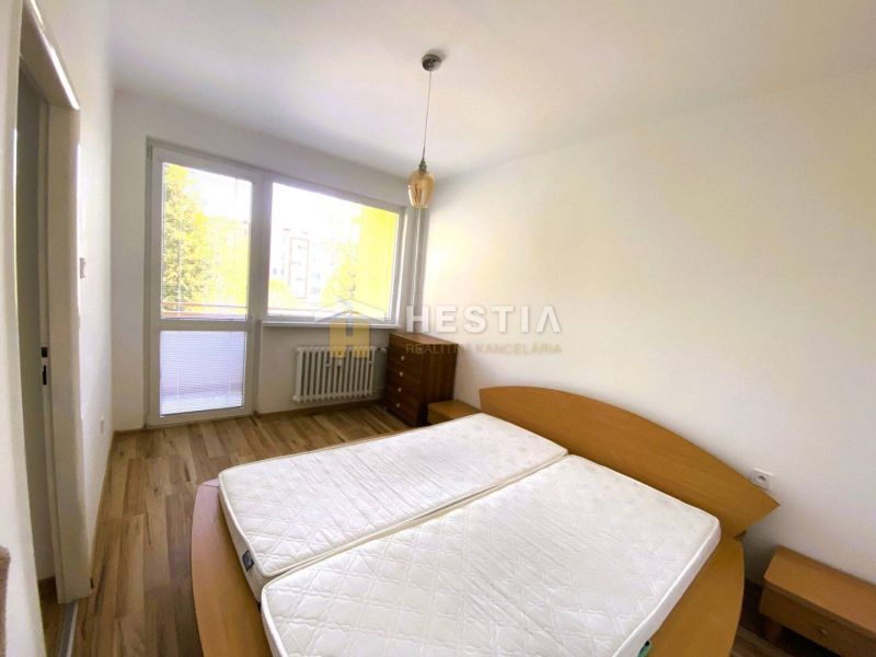Bedroom in a two-room apartment with a wood-patterned floor and a large window.