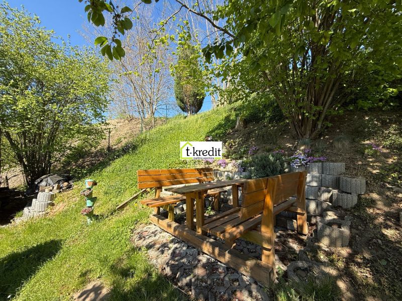 A garden in Čaradice by a family house with wooden seating under a tree.