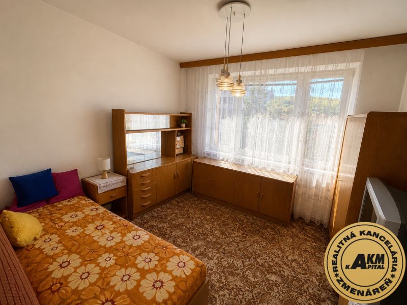 A room with a bed and a wardrobe in a 3-room apartment with a floral carpet.