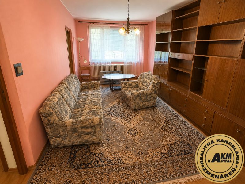 Living room in a 3-room apartment with pink walls, patterned carpet, and wooden cabinets.