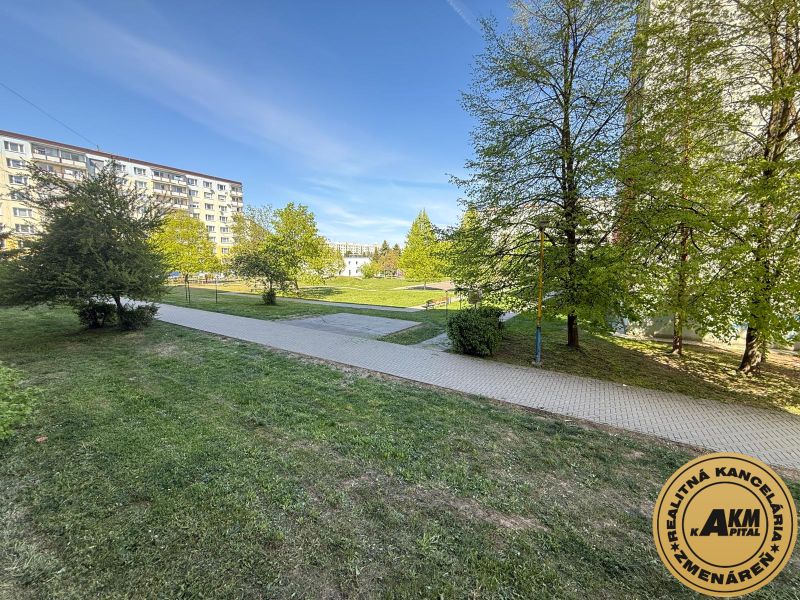 Grassy area with a sidewalk and apartment buildings on Tulská Street in Zvolen.