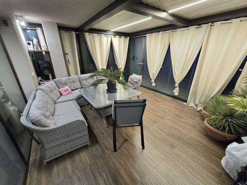 A covered terrace of a family house with a corner sofa and a floor with a wooden decor.