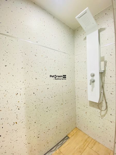 A bathroom with a shower and a wooden decor floor in a 2-room apartment.