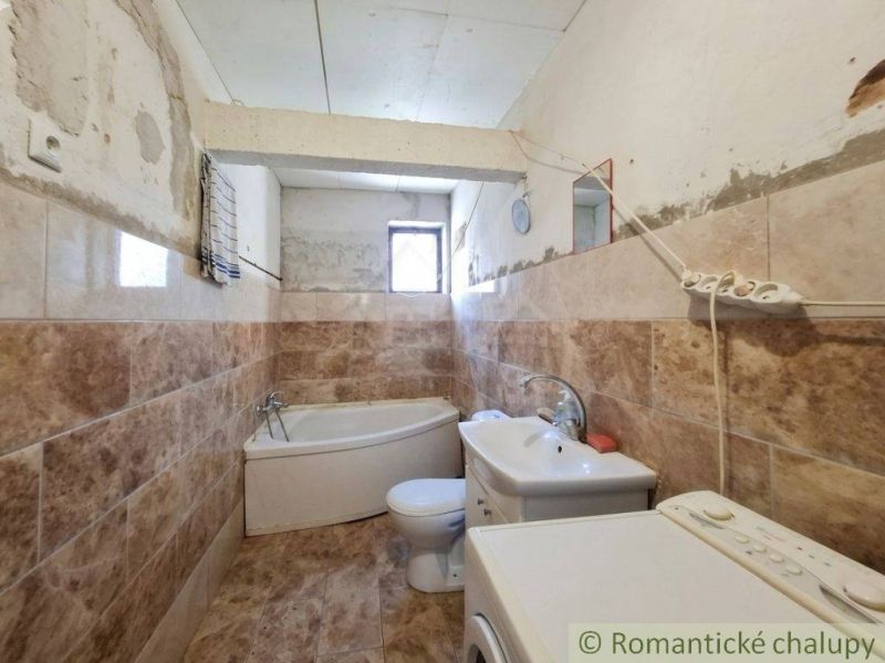 A bathroom in a family house with a bathtub and a washing machine, tiled with ceramic tiles.