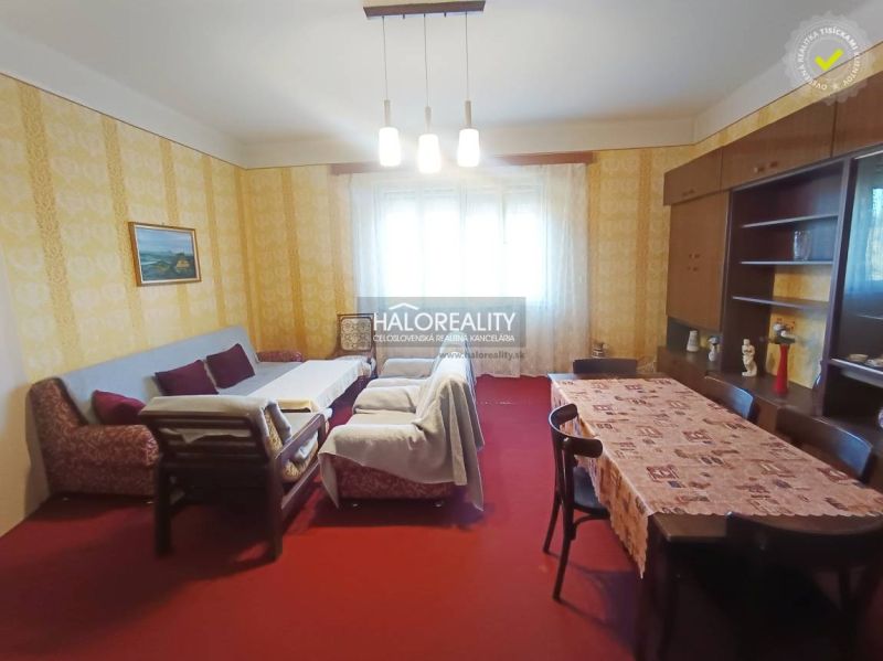Living room of a two-room apartment with a sofa, dining table, and red carpet.