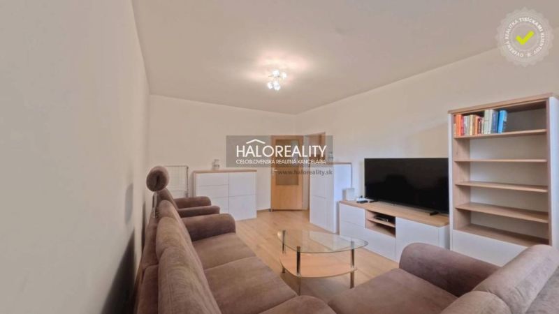 Living room in a two-room apartment with a sofa, television, and wooden decor flooring.