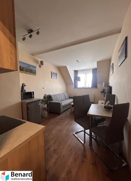 Living area of a 2-room apartment with a sofa, dining table, and wooden decor flooring.