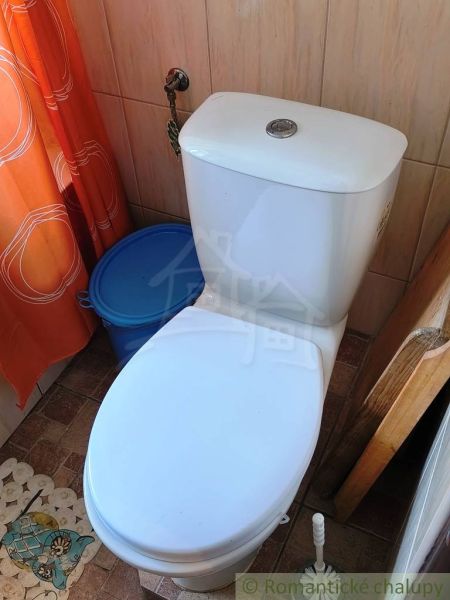 A toilet in a family house, with an orange curtain and a blue bucket.