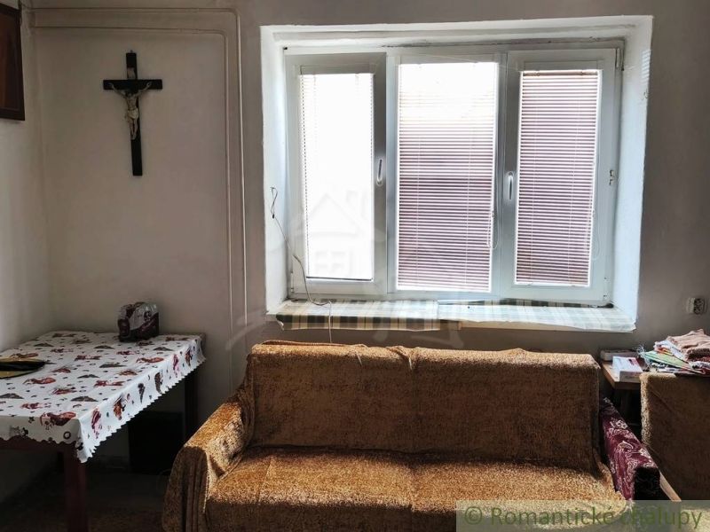 A room in a family house with a sofa, a table with a cloth, and a cross on the wall.