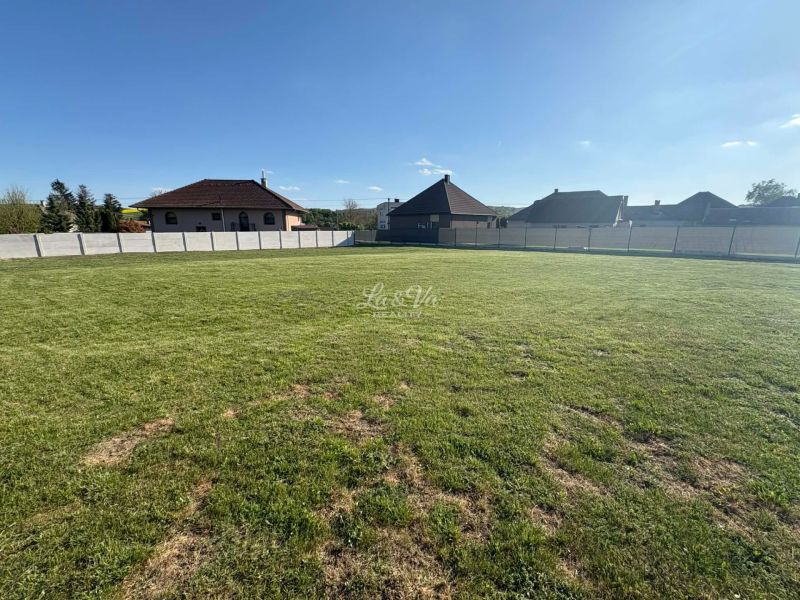 A residential plot in Pozba with a grassy area and surrounding houses.
