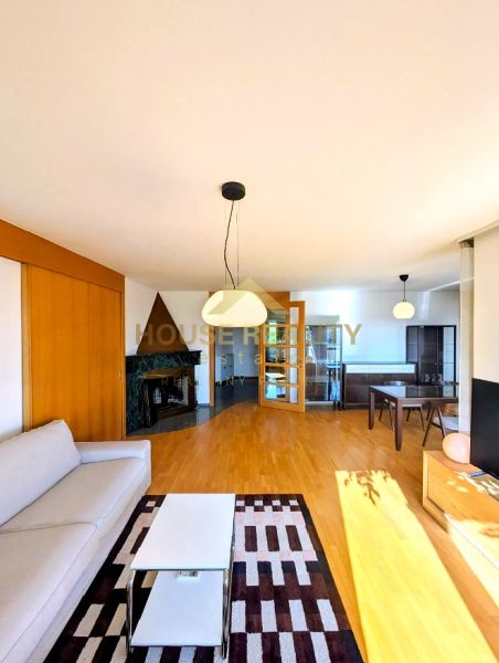 Living room in a 4-room apartment with a fireplace, sofa, and wooden decor flooring.