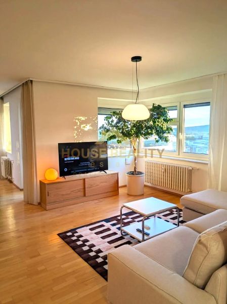 Living room in a 4-room apartment with a wood-decor floor, sofa, and television.
