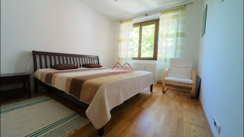 Bedroom in a 2-room apartment with wood-patterned flooring, a bed, and a chair.
