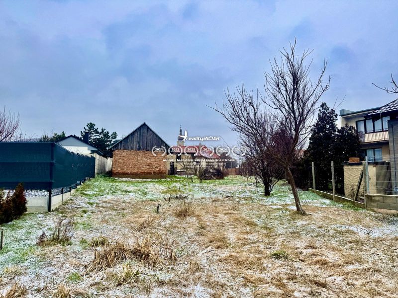 A snowy plot with a house without a facade in Dvorníky, fencing, grassy terrain, blades of grass.