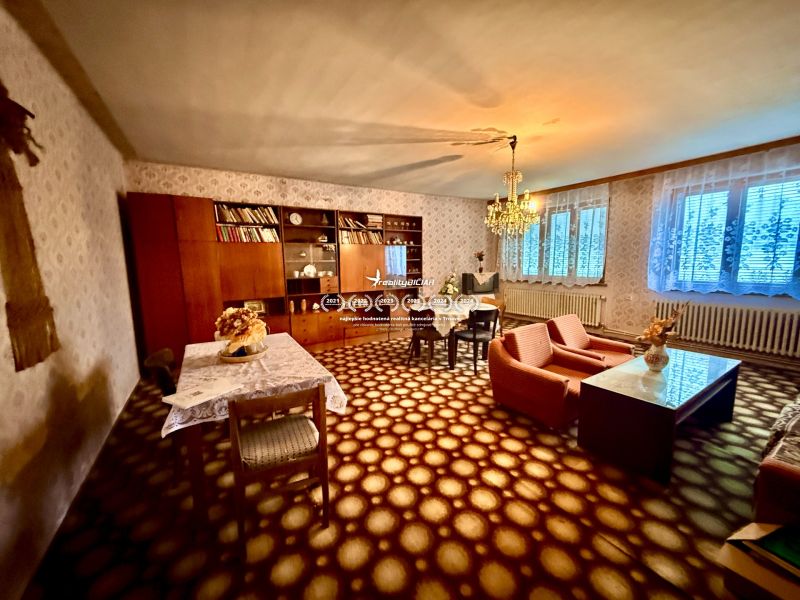A living room in a family house with carpeted flooring, retro furniture, and a chandelier.