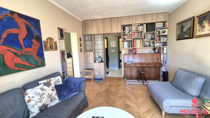 Living room in a two-room apartment with a piano, sofas, and a wooden decor floor.