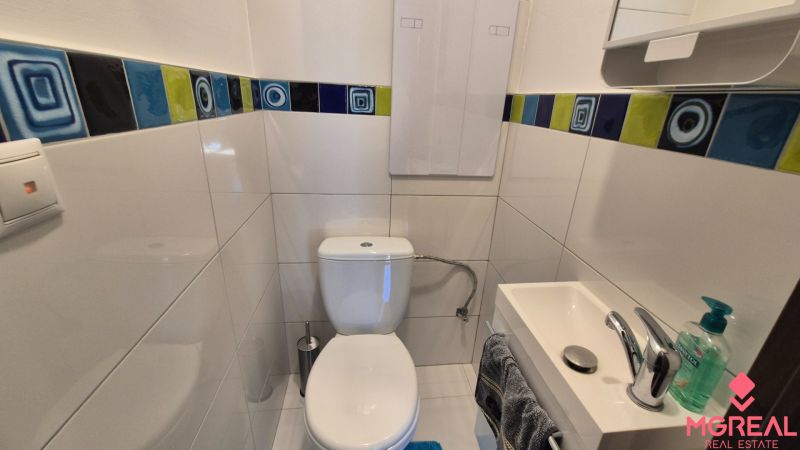 A bathroom in a 2-room apartment with white tiles and a colorful strip of tiles.