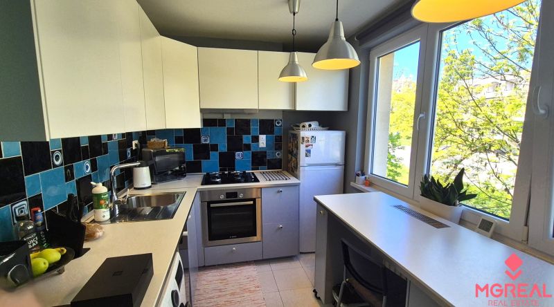 A kitchen in a 2-room apartment with blue-black tiles and large windows.