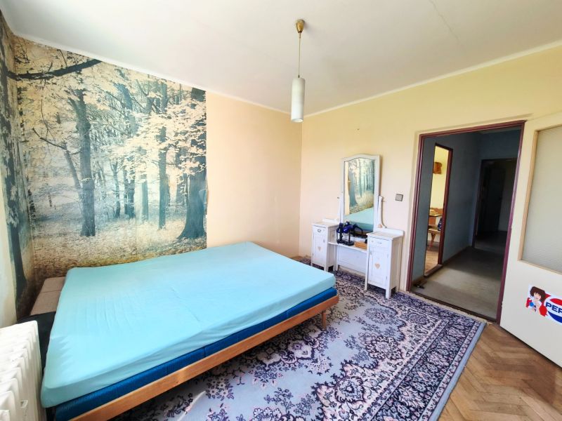 A bedroom in a 3-room apartment with a forest wallpaper and a wooden decor floor.