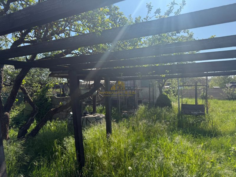 A garden by the cottage in Malacky with a gazebo and a swinging bench surrounded by tall grass.
