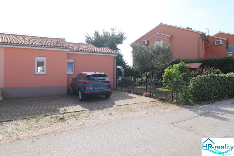 A family house in the town of Vodice, parking space, and a garden with flowers and trees.