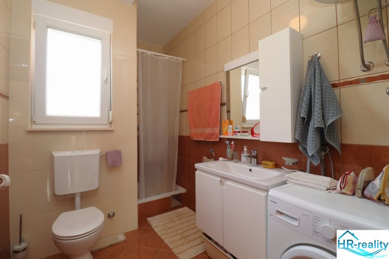 A bathroom in a family house with a sink, a washing machine, and a shower stall.