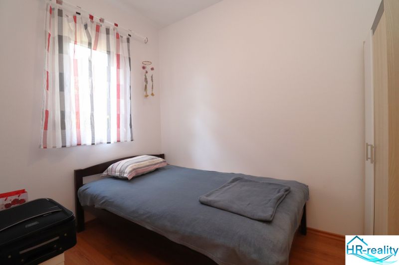 Simple bedroom with a bed, wood-patterned flooring, and light curtains.