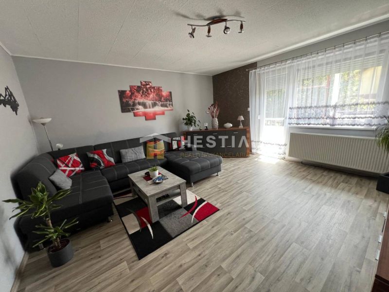 A spacious living room in a three-room apartment with a wooden decor floor and a comfortable sofa set.