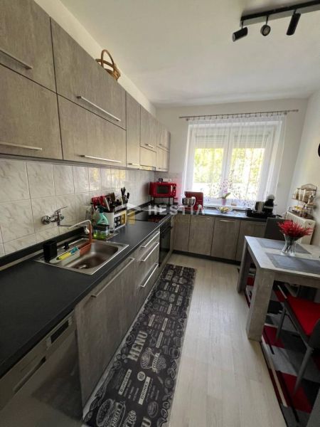 A kitchen with a kitchen unit, table, and floor with a wooden decor in a 3-room apartment.