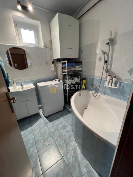 A compact bathroom in a 3-room apartment with a bathtub, sink, washing machine, and storage space.
