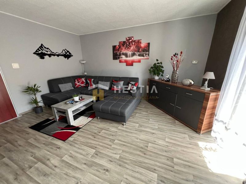 Living room in a three-room apartment with a wooden decor floor and a gray sofa.