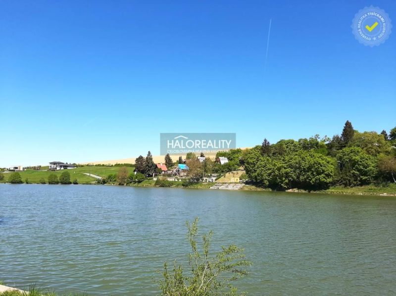 A body of water and houses around the gardens in Hubina, surrounded by greenery and a blue sky.