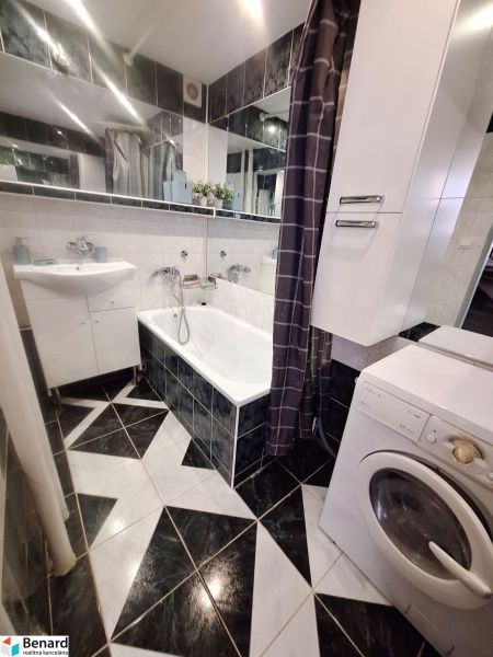 A bathroom with black and white tiles, a sink, a bathtub, and a washing machine in a studio apartment.
