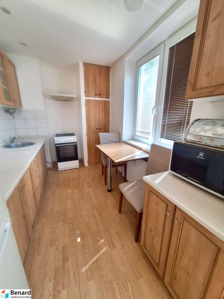A kitchen in a studio apartment with furniture and flooring featuring a wood design.