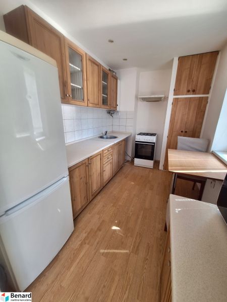 A kitchen in a studio apartment with white walls, a wood-patterned floor, and appliances.
