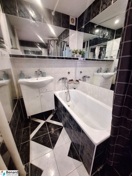 Bathroom in a studio apartment with a bathtub, sink, and dark tiles.