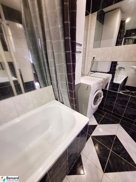 A bathroom in a studio apartment with a bathtub, washing machine, and black-and-white tiles.