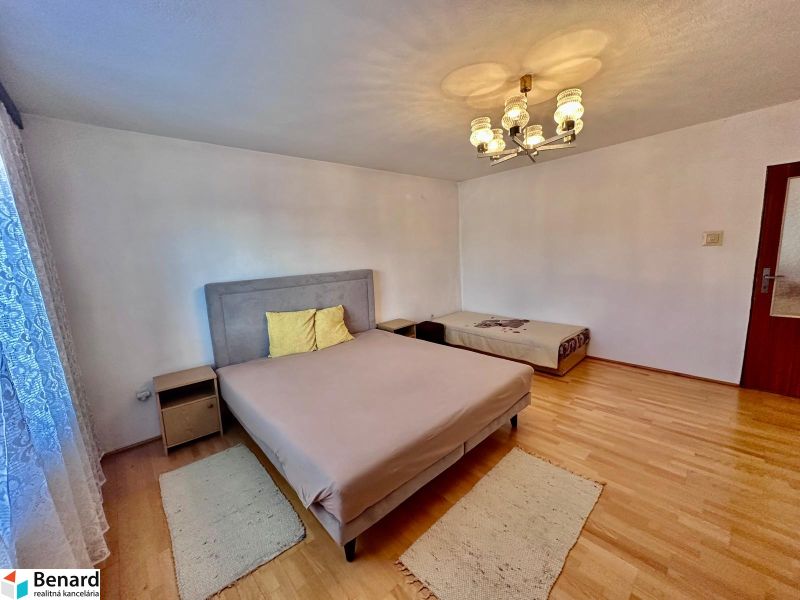 A bedroom with two beds, a wooden decor floor, a bright chandelier, a carpet.