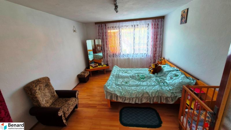 A room in a family house with a bed, an armchair, and a floor with a wooden decor.