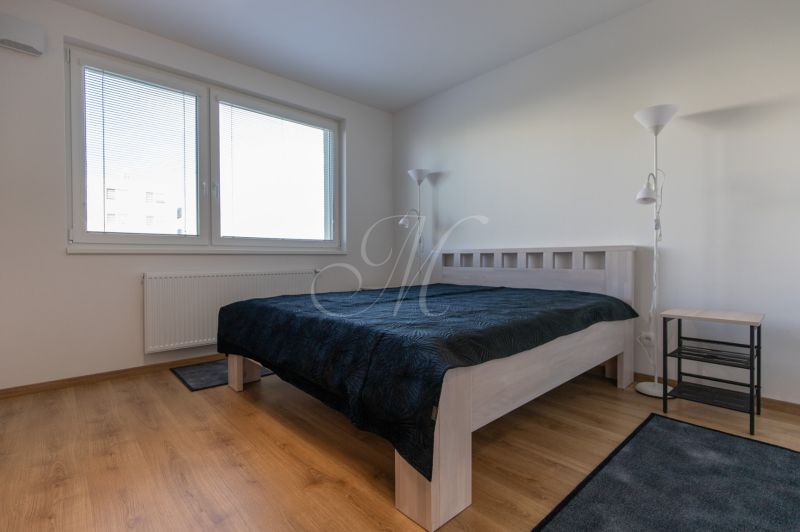 Bedroom in a 2-room apartment with a bed, lamp, and wooden decor flooring.
