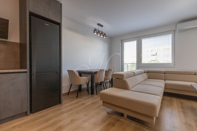 Living room with a leather sofa, dining table, and wooden decor flooring in a 2-room apartment.
