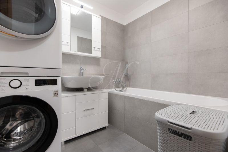 Bathroom in a 2-room apartment with a washing machine, sink, bathtub, and storage space.