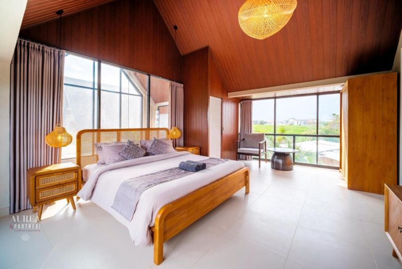Bedroom in a villa with large windows, wooden elements, and a bed with linen.