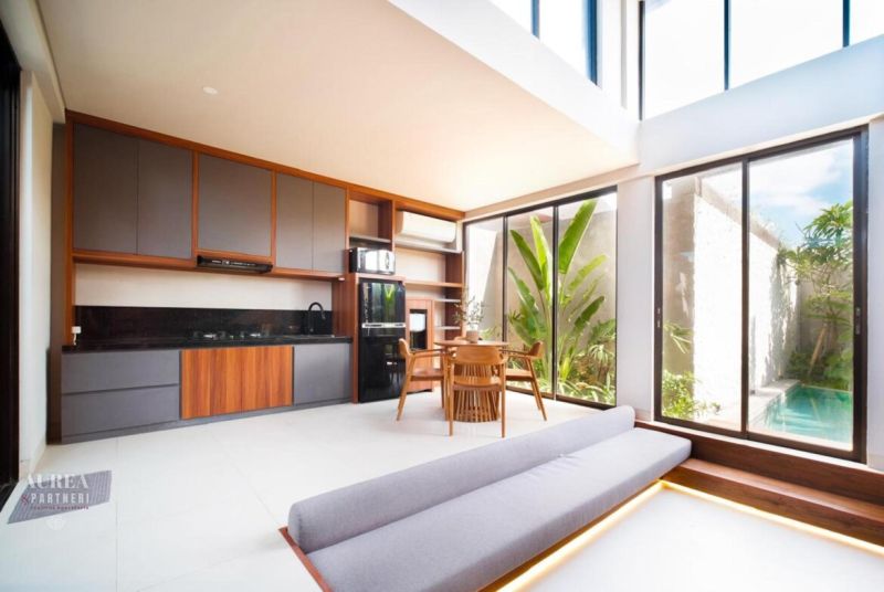 A villa with a wooden decor floor, kitchen, and dining area. Large windows provide a view of the garden.
