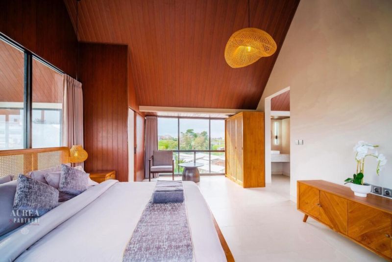 Interior of a villa with a large bed, wooden decor, and a large window.
