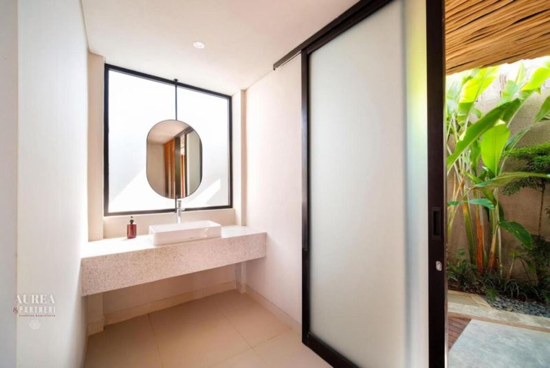A bathroom in a villa with a sink, a round mirror, and sliding doors.