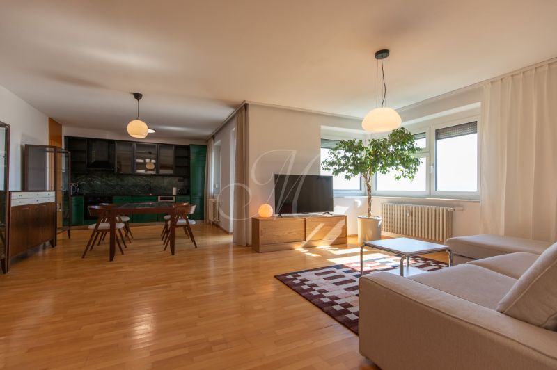 Living room in a 4-room apartment with a wood-patterned floor and furniture in the kitchen.