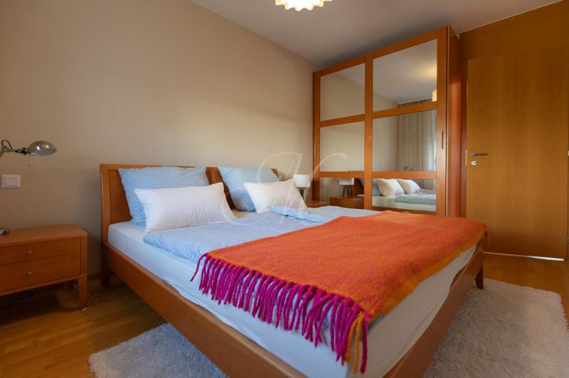 Bedroom in a 4-room apartment with a bed, mirrored wardrobe, and wooden decor flooring.