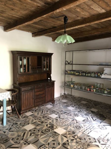 Interior of a family house with a wooden ceiling and patterned tiles, a cabinet, and shelves with glasses.